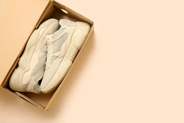 Cardboard box with sports shoes on beige background