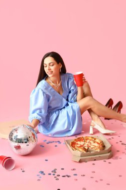 Fincanlı genç kadın, lezzetli pizza ve pembe arka planda disko topu.
