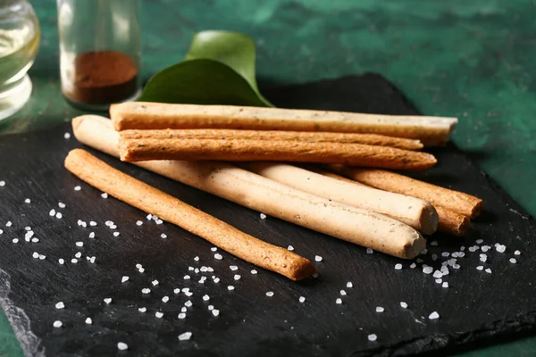 stock image Slate board with tasty Italian Grissini on green background, closeup