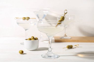 Beyaz ahşap masada zeytinli bir bardak martini.