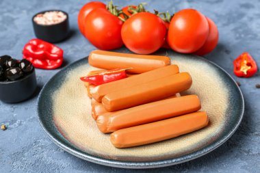 Mavi arka planda sosis, domates ve zeytinli tabak.