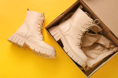 Sarı arka planda şık ayakkabılar olan karton kutu.