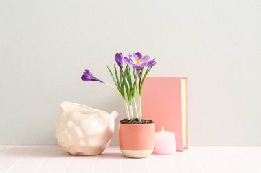 Güzel çiçekli tencere, dekoratif deniz kabuğu, kitap ve yanan mum beyaz duvarın yanındaki masada.