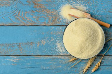 Bir kase çiğ irmik ve mavi ahşap arka planda dikenler.