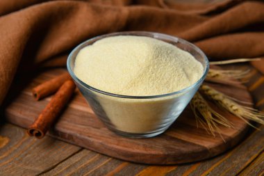 Ahşap arka planda bir kase çiğ irmik, tarçın ve dikenli çivi.