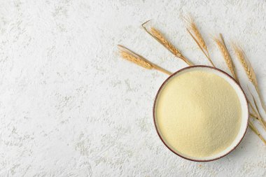 Beyaz arka planda bir kase çiğ irmik ve dikenler.