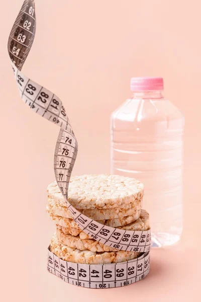Rice cakes, bottle of water and measuring tape on pink background. Diet concept
