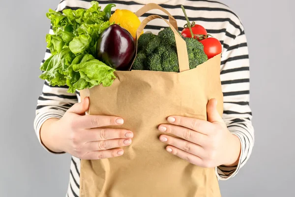 灰色の背景に野菜や果物を入れた紙袋を持った女性 — ストック写真