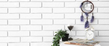 Işık tuğlası duvarda asılı şık bir düş kapanı çalar saat, kum saati ve moda dergileriyle dolu bir masa. Tasarım için pankart