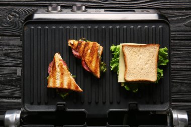 Siyah ahşap arka planda modern elektrikli ızgarada lezzetli sandviçler.