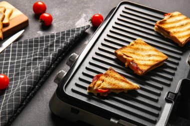 Siyah grunge arka planda lezzetli sandviçleri olan modern elektrikli ızgara.