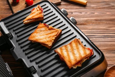 Ahşap masada lezzetli sandviçleri olan modern elektrikli ızgara.