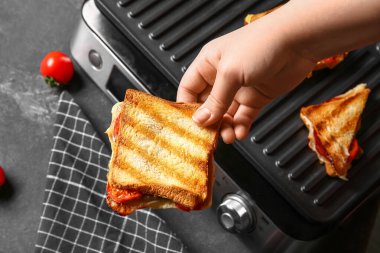 Modern elektrikli ızgaranın yanında nefis bir sandviç tutan kadın.