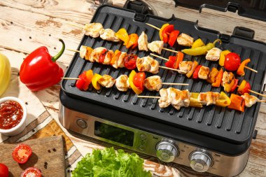 Lezzetli tavuk şişleri ve hafif ahşap arka planda sebzeli modern elektrikli ızgara.