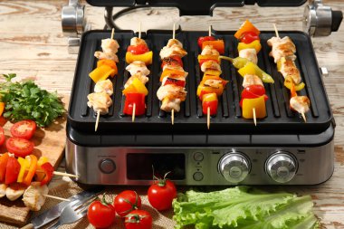 Lezzetli tavuk şişleri ve hafif ahşap arka planda sebzeli modern elektrikli ızgara.