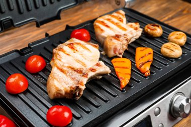 Ahşap arka planda lezzetli biftekli ve sebzeli modern elektrikli ızgara.