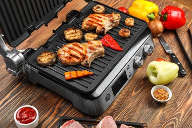 Ahşap arka planda lezzetli biftekli ve sebzeli modern elektrikli ızgara.