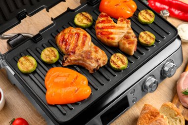 Ahşap arka planda lezzetli biftek ve sebzeli modern elektrikli ızgara, yakın plan.