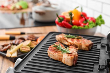 Hafif tuğla duvarın yanındaki masada lezzetli biftekleri olan modern elektrikli ızgara. Yakın plan.