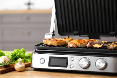 Mutfaktaki masada lezzetli biftekleri ve sebzeleri olan modern elektrikli ızgara.