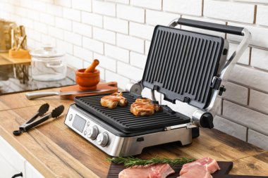 Beyaz tuğla duvarın yanındaki masada lezzetli biftekleri olan modern elektrikli ızgara.