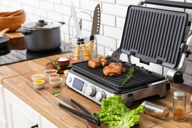 Beyaz tuğla duvarın yanındaki masada lezzetli biftekleri olan modern elektrikli ızgara.