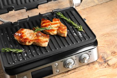 Ahşap arka planda lezzetli biftekleri olan modern elektrikli ızgara.