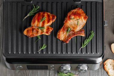 Ahşap arka planda lezzetli biftekleri olan modern elektrikli ızgara.