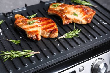 Karanlık arka planda lezzetli biftekleri olan modern elektrikli ızgara.