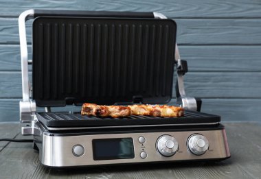 Gri ahşap masada lezzetli biftekleri olan modern elektrikli ızgara.