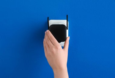 Mavi duvardaki elektrik prizine siyah kablosuz ağ yineleyiciyi takan kadın