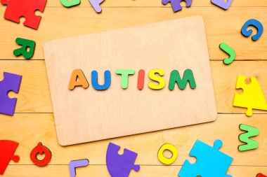 Tahta zemin üzerinde harfler ve yapboz parçaları olan kelime AUTISM