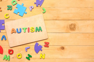 Tahta zemin üzerinde harfler ve yapboz parçaları olan kelime AUTISM