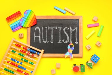 Sarı arka planda kelime AUTISM ve bebek oyuncakları ile tebeşir tahtası