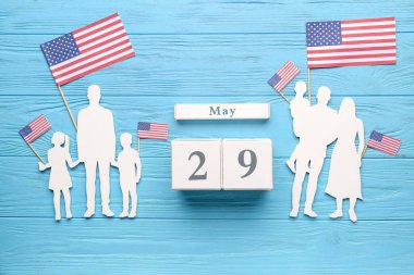 Aile figürleri ve mavi ahşap arka planda ABD bayraklarıyla Anma Günü