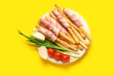 Sarı arka planda domuz pastırmalı İtalyan Grissini tabağı.