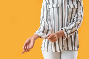 Young woman rolling up her sleeve on yellow  background