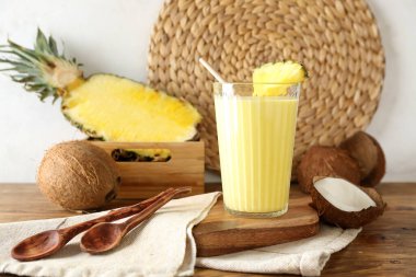 Ahşap masada bir bardak lezzetli ananas suyu, saman ve hindistan cevizi.