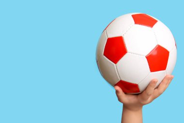 Açık mavi arka planda futbol topuyla çocuk eli
