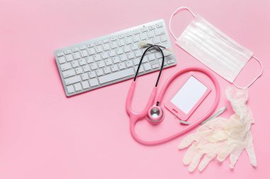 Stetoskop, klavye, rozet, tıbbi maske ve pembe arka planda lastik eldivenler.