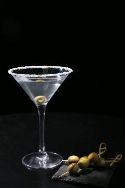 Siyah arka planda zeytinli bir bardak lezzetli martini.