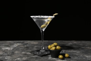 Koyu arkaplanda zeytinli bir bardak martini.
