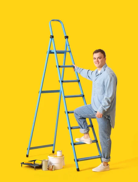 Sarı Arka Planda Merdiveni Boya Kutuları Olan Genç Bir Adam — Stok fotoğraf