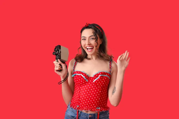 Young pin-up woman with retro video camera on red background