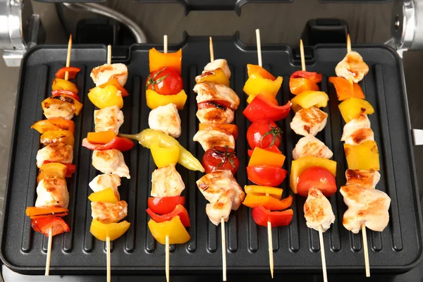 Modern electric grill with tasty chicken skewers and vegetables on table