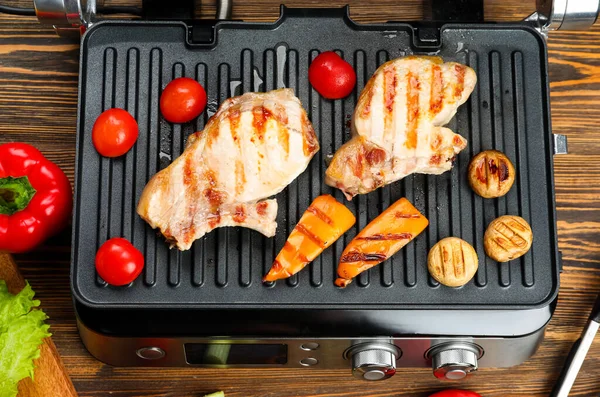 stock image Modern electric grill with tasty steaks and vegetables on wooden background