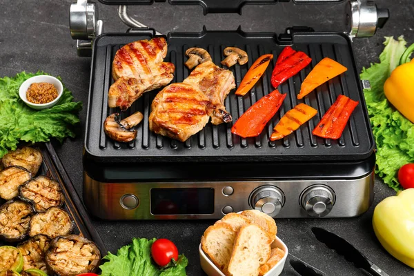 stock image Modern electric grill with tasty steaks and vegetables on dark background