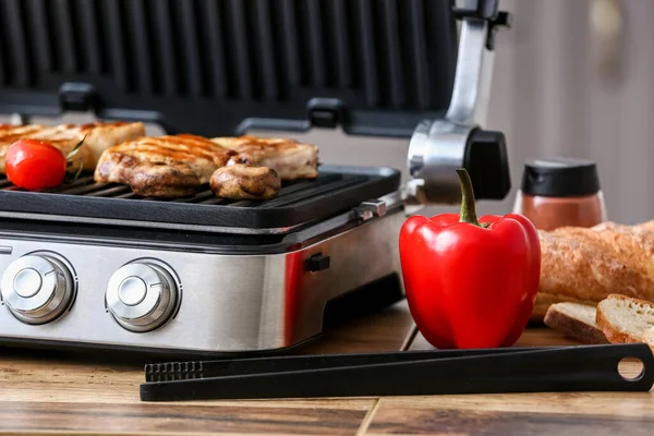 Modern electric grill with vegetables and tasty steaks in kitchen, closeup