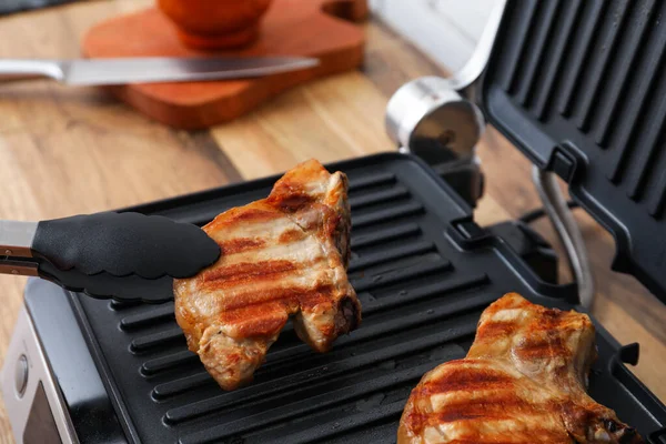 Modern electric grill with tasty steaks on table, closeup