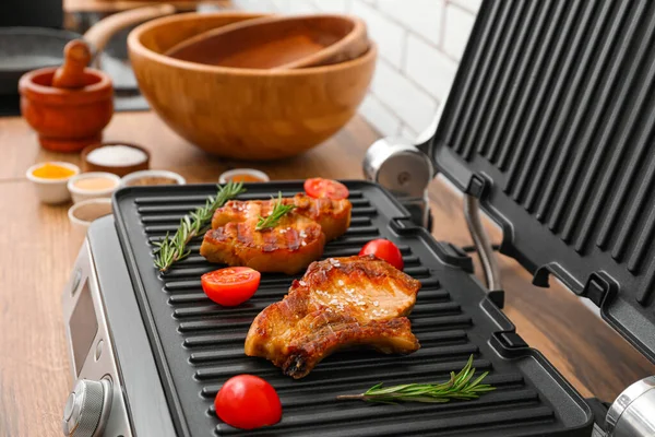 stock image Modern electric grill with tasty steaks and tomatoes on table near white brick wall